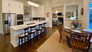 A modern kitchen with white cabinetry, a marble island, and a dining area with wooden chairs.