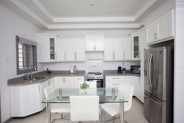 Una cocina moderna con armarios blancos, un refrigerador de acero inoxidable y una mesa de comedor de vidrio.
