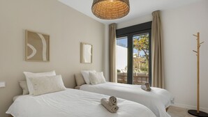 Een hotelkamer met twee bedden, een groot raam met uitzicht op het omliggende landschap, een geweven plafondlamp en een kapstok.