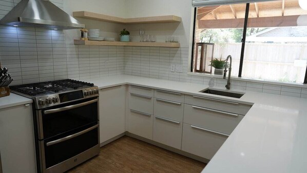 Una cocina con gabinetes blancos, una estufa de acero inoxidable y una ventana con vista al jardín trasero.