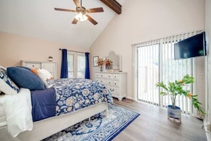 Un dormitorio con cama, cómoda, televisor, ventilador de techo y ventana con persianas.
