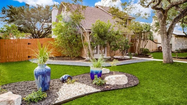 Un jardin bien entretenu, avec une pelouse, des vases décoratifs et une clôture en bois.