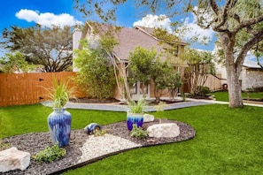 Un jardín bien cuidado con césped, jarrones decorativos y una valla de madera.