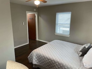 A bedroom with a bed, a window, a door, and a ceiling fan.
