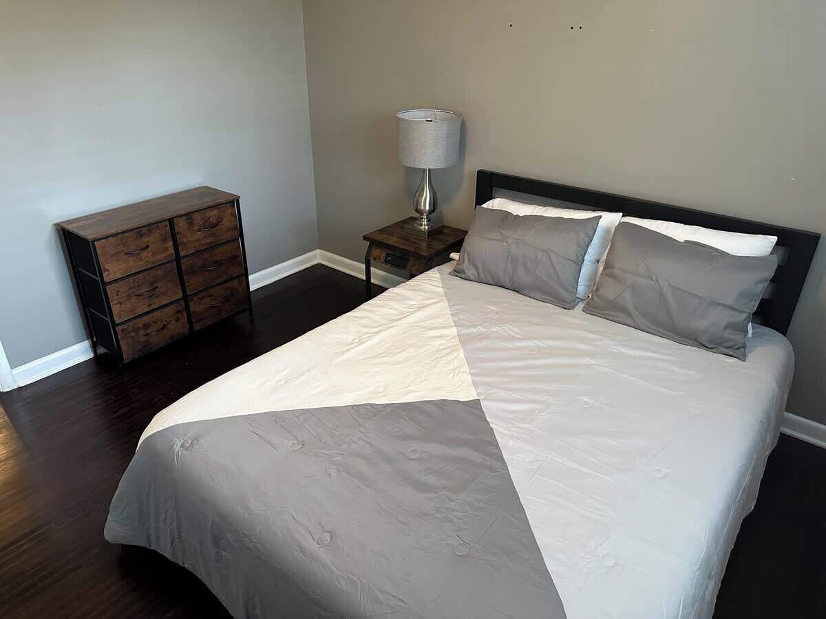 A bedroom with a bed, a nightstand, a lamp, and a dresser.