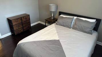 A bedroom with a bed, a nightstand, a lamp, and a dresser.