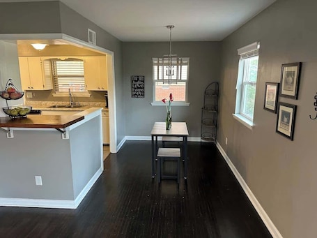 A modern kitchen with a central island, a dining area with a table and chairs, and a hallway with framed pictures on the walls.. Renovated 3BR House in Little Rock
