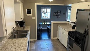 Una cocina con encimeras de granito, un lavamanos de acero inoxidable, un refrigerador negro y un ventilador de techo.