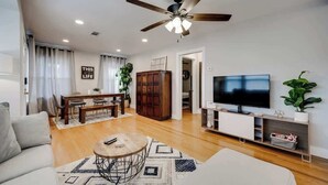A modern living room with a sofa, a coffee table, a TV, a ceiling fan, and a dining area with a table and chairs. - Stylish Retreat Near Hot Springs Attractions (Hot Springs)