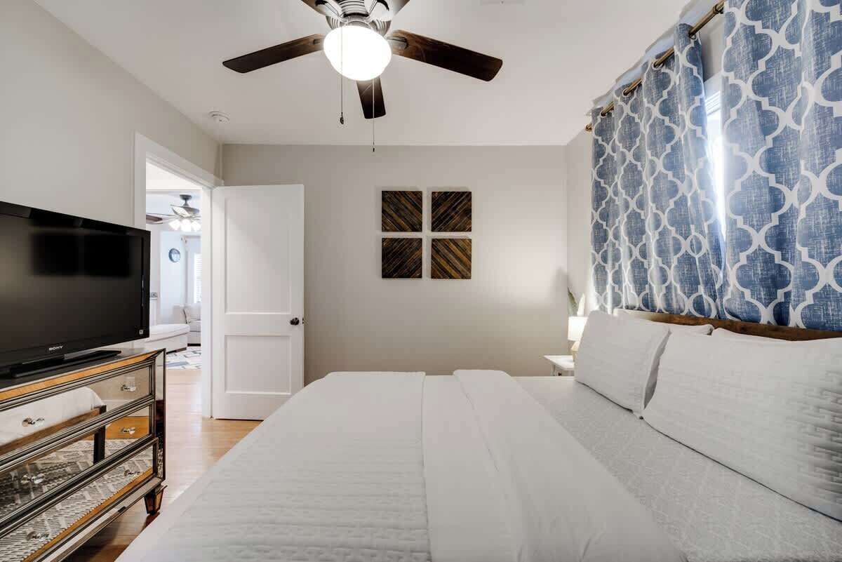 A bedroom with a bed, a ceiling fan, a television, and a wall-mounted artwork.