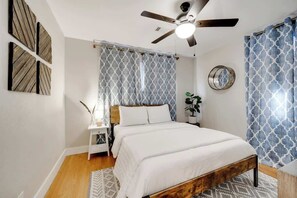 Une chambre à coucher avec un lit, un ventilateur de plafond, une table de chevet, un miroir et des rideaux à motifs.
