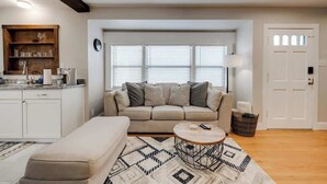A living room with a sofa, a coffee table, and a kitchen area with cabinets and a window. - Stylish Retreat Near Hot Springs Attractions (Hot Springs)