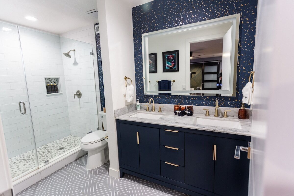Un baño moderno con ducha de vidrio, inodoro blanco y muebles de color azul oscuro con tiradores dorados.