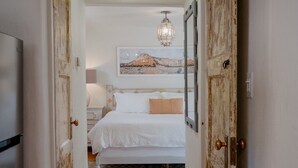 Un pasillo que conduce a un dormitorio con una cama, una araña y un cuadro en la pared.