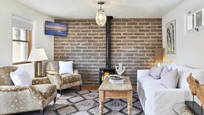 Una sala de estar con pared de ladrillo, chimenea, sofá, sillones y una mesa de centro.
