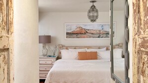 Un dormitorio con cama, mesita de noche, lámpara y un cuadro en la pared.