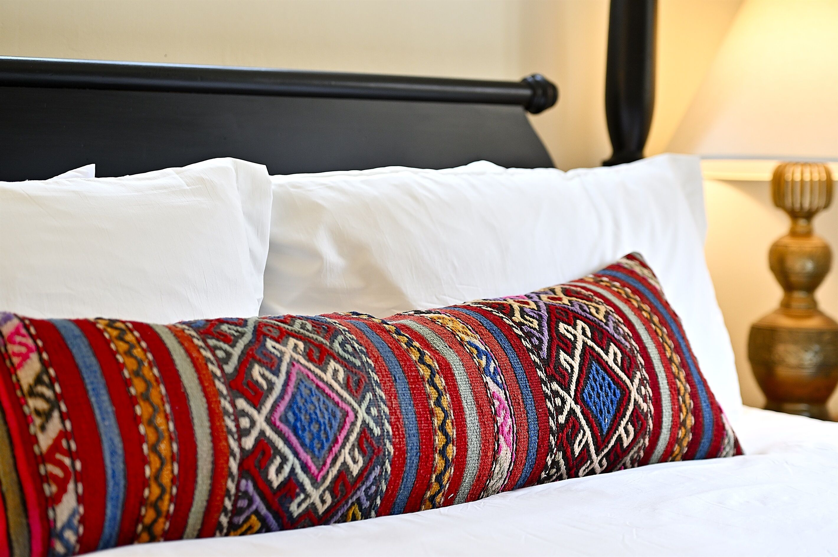 A bed with white pillows and a colorful, patterned pillow.