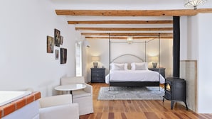 Un dormitorio con cama, mesitas de noche, una pequeña mesa redonda, un sofá, suelo de madera, lámpara colgante y estufa negra.