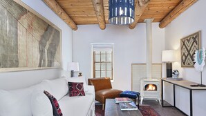 A cozy living room with a white sofa, a brown leather chair, a small table with books, a fireplace, and a large abstract painting on the wall. - Dos Hermanas 4, 5, 6 & 8| Walk to Plaza| Courtyard (Santa Fe)
