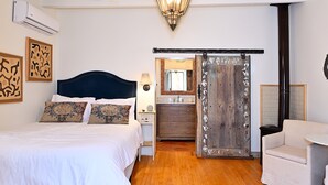 A bedroom with a bed, bedside table, lamp, and a wooden door with decorative elements. - Dos Hermanas 4, 5, 6 & 8| Walk to Plaza| Courtyard (Santa Fe)