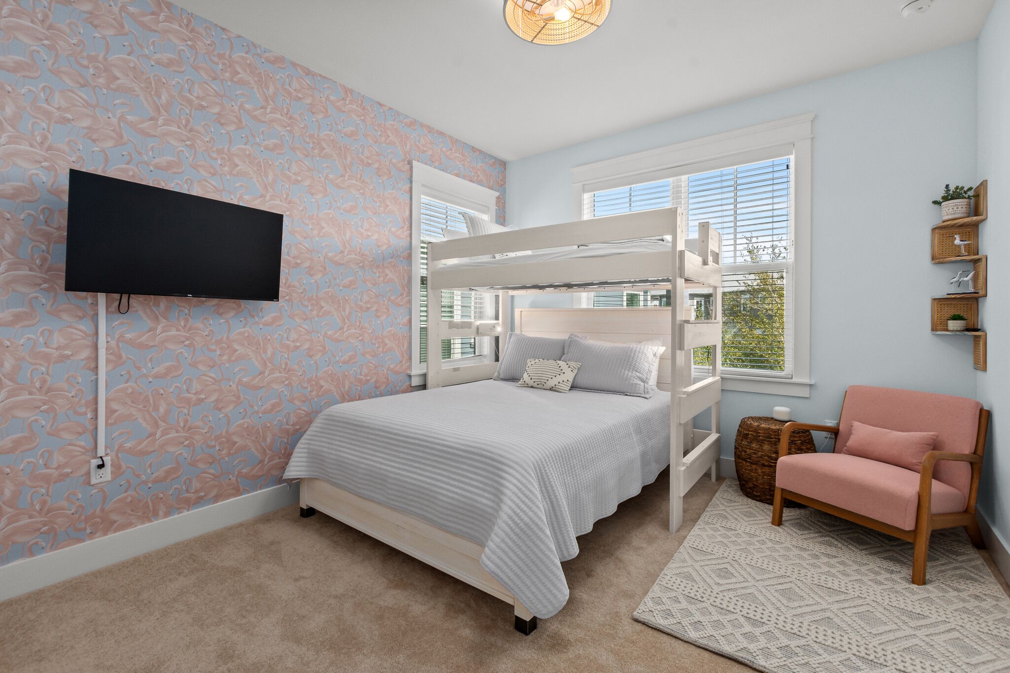 Une chambre avec un lit superposé, un téléviseur à écran plat, un fauteuil rose et un mur décoratif.