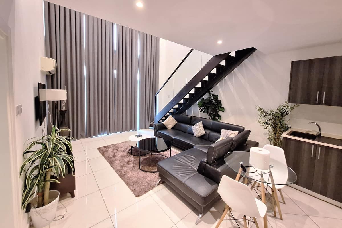 A modern living room with a sofa, coffee table, and a glass dining table. There is a staircase leading to another level.