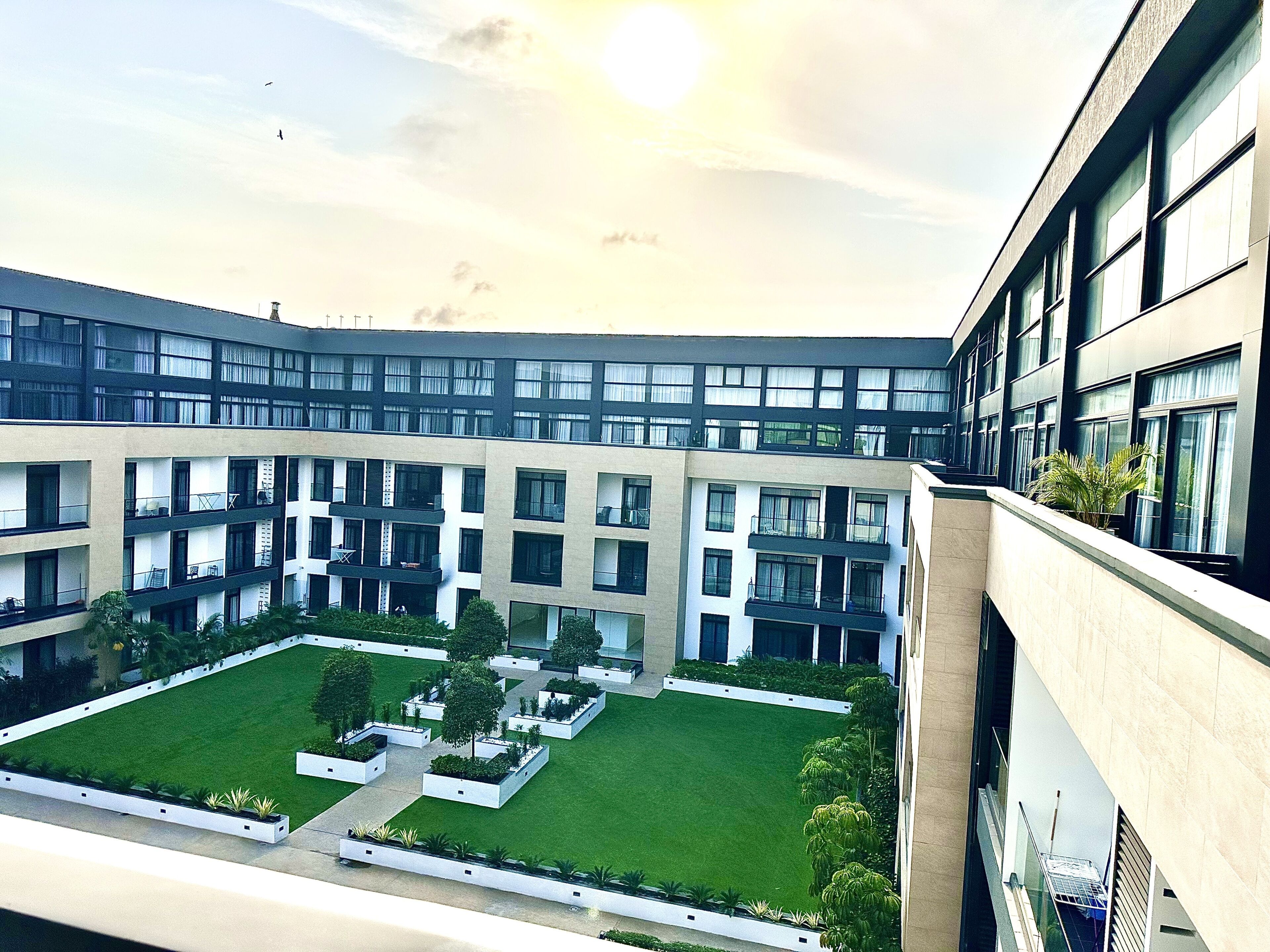 A modern building with multiple floors, large windows, and a central courtyard with grass and plants.