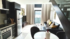 A modern kitchen with a built-in oven and refrigerator, a dining area with a round table and chairs, and a living area with a sofa and a coffee table. - Embassy Gardens Apartment (Accra)