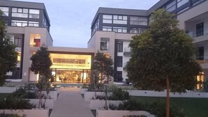 A modern building with a central glass facade, surrounded by landscaped areas and trees. - Embassy Gardens Apartment (Accra)