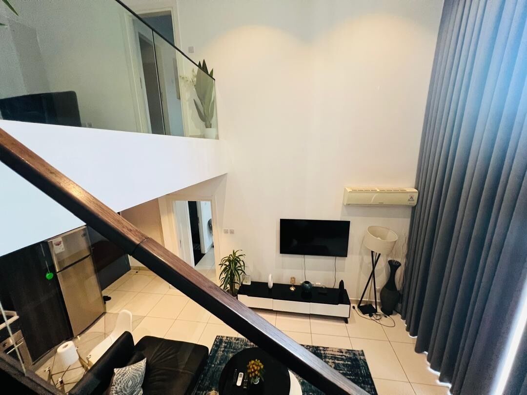 A modern living room with a flat-screen TV, a sofa, a coffee table, and a staircase leading to an upper level.