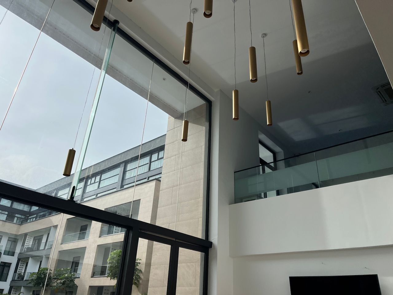 A modern interior with large windows, a glass railing on the upper level, and hanging pendant lights.