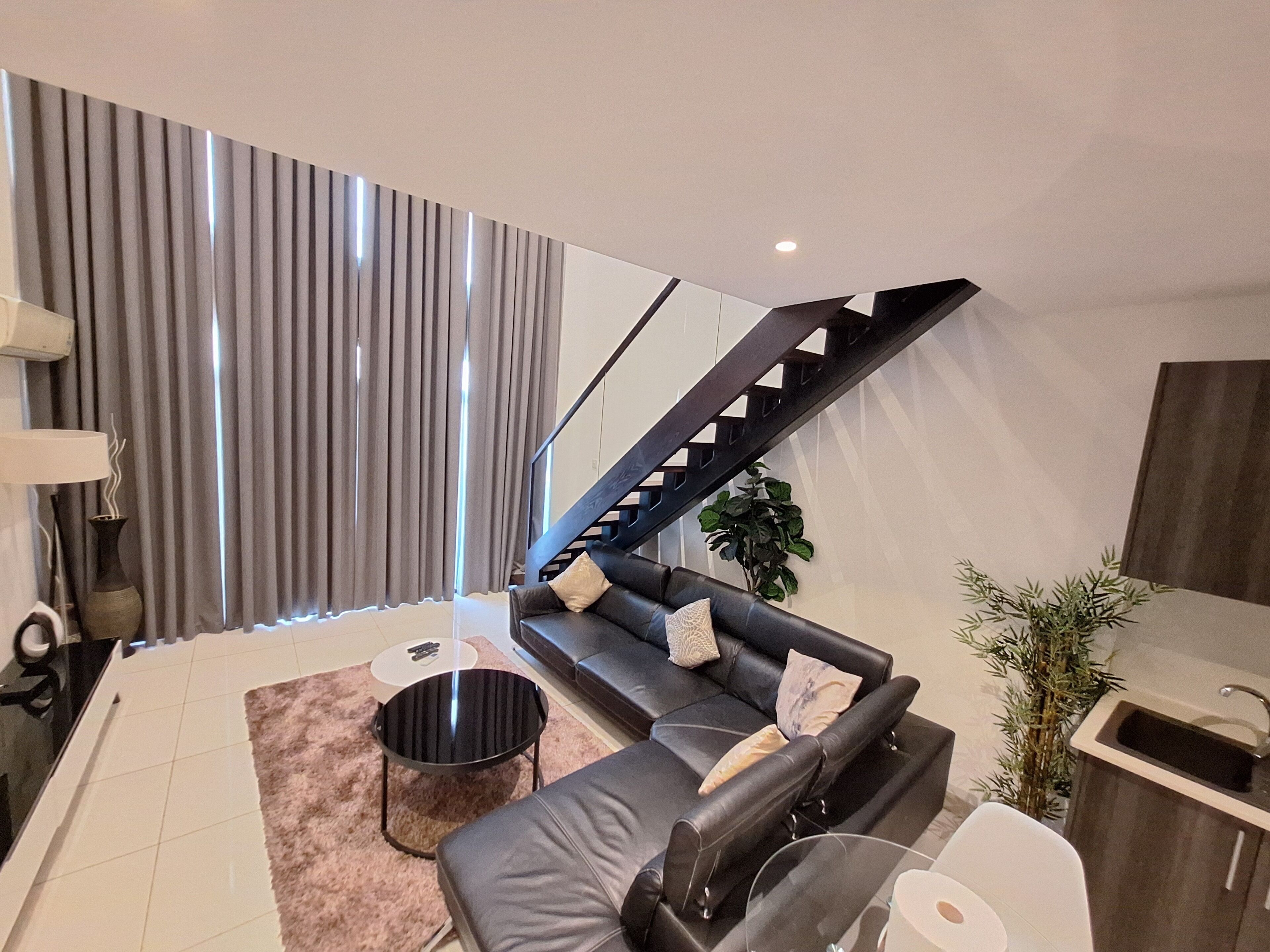 A modern living room with a black leather sofa, a round coffee table, and a staircase leading to an upper level.