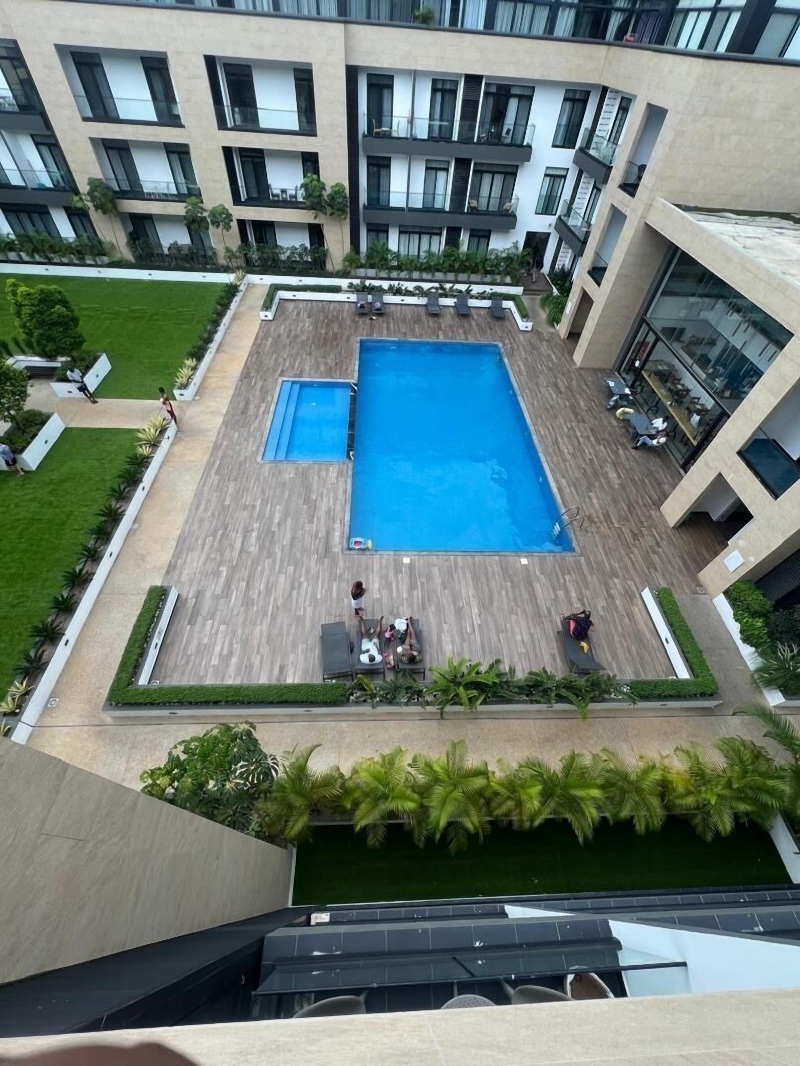 Un área de piscina en la azotea con una piscina rectangular grande, rodeada de sillas de descanso y una terraza de madera.