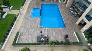 Un área de piscina en la azotea con una piscina rectangular grande, rodeada de sillas de descanso y una terraza de madera.