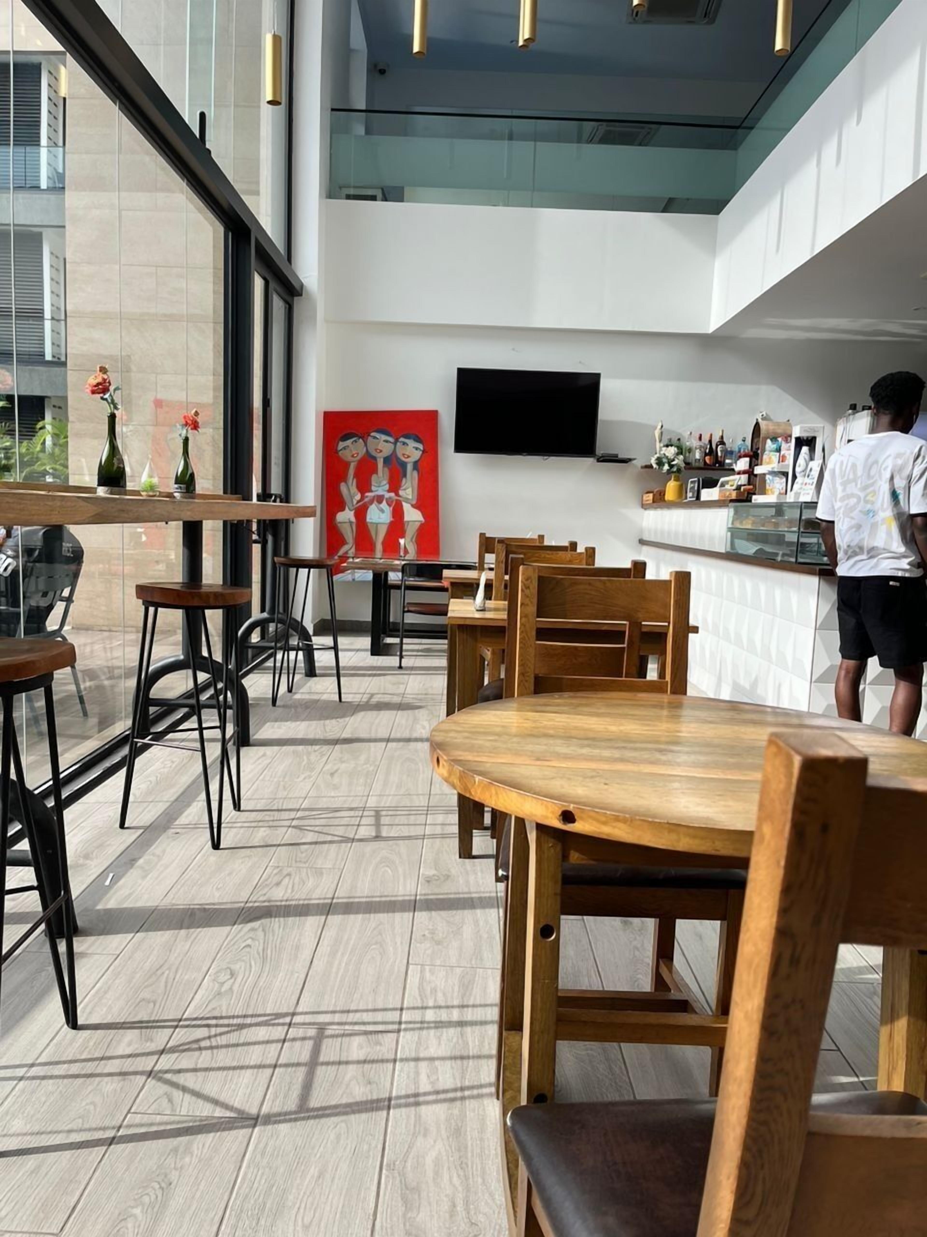 A modern restaurant with wooden tables and chairs, a large window, and a flat-screen TV on the wall.