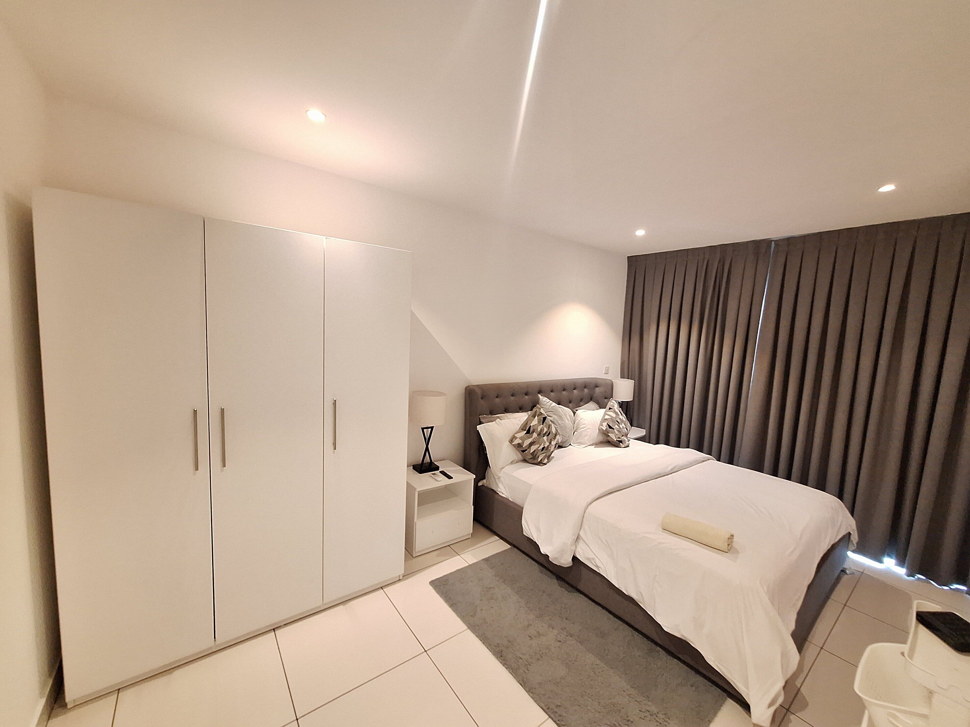 Un dormitorio moderno con un armario grande, una cama con cabecero y una mesita de noche.