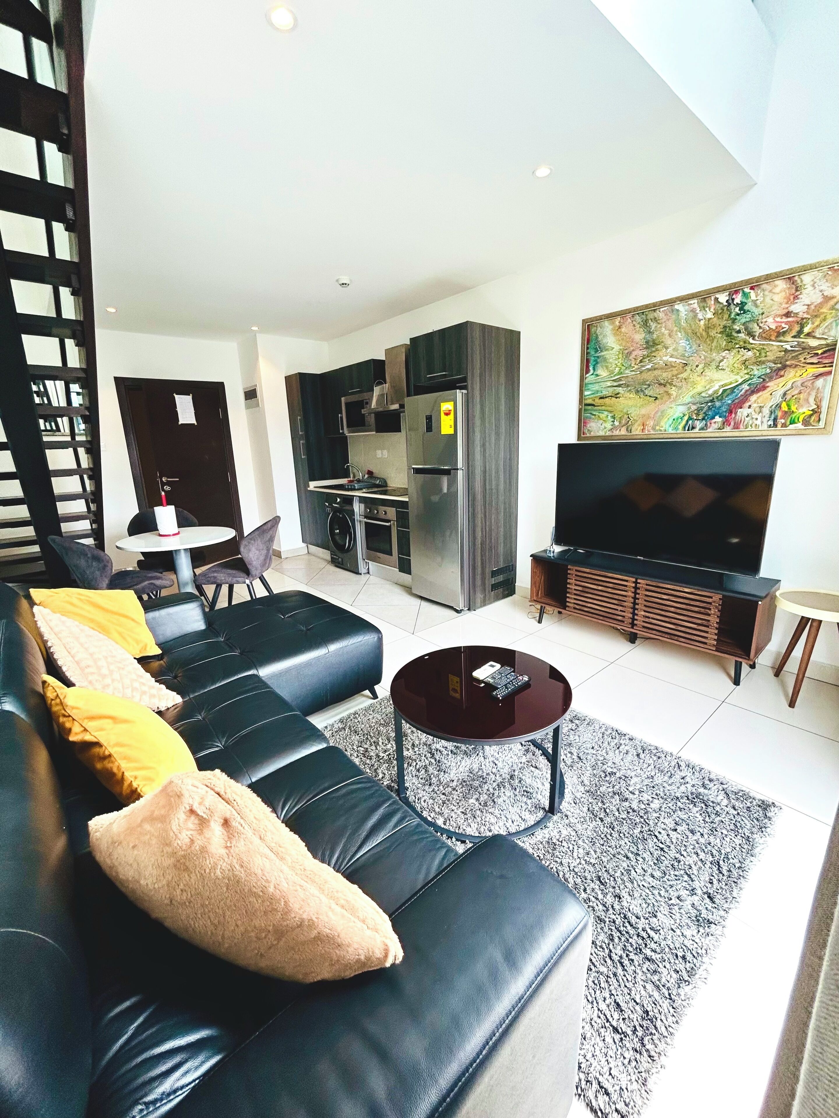 A modern living room with a black leather sofa, a round coffee table, and a flat-screen TV.