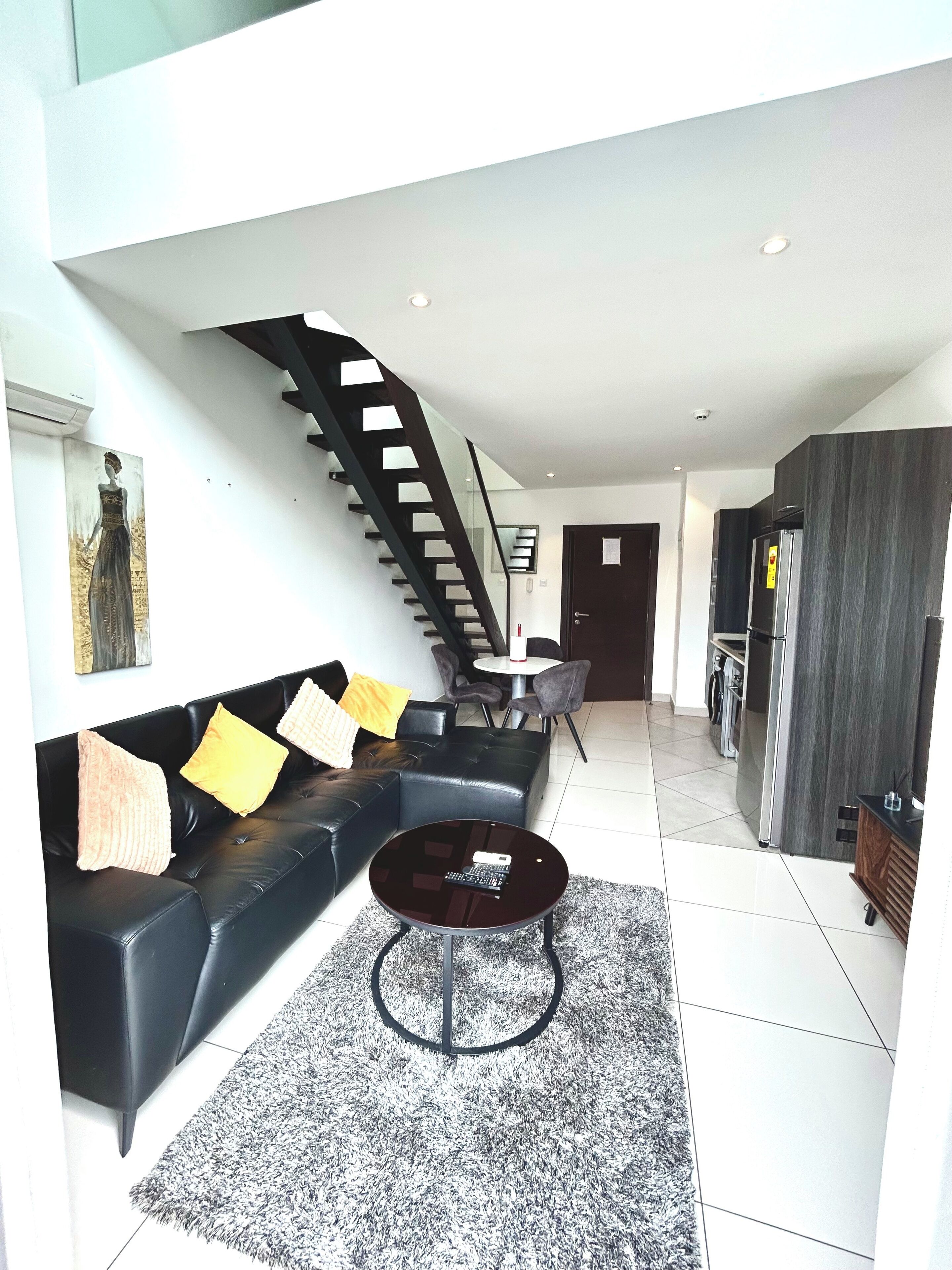 A modern living room with a black leather sofa, a round coffee table, and a staircase leading to another level.