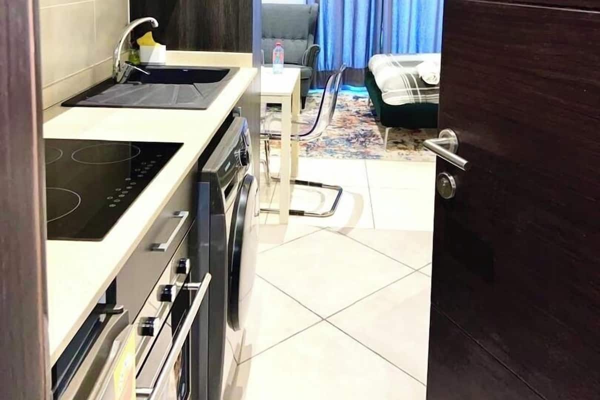 A compact kitchen with modern appliances, a dining area with a table and chairs, and a view of a living room with a sofa and curtains.