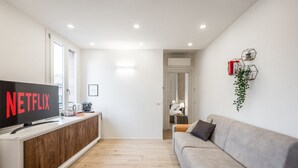 Ein modernes Wohnzimmer mit Flachbildfernseher, einer Couch, einem Holzschrank und einer Pflanze.