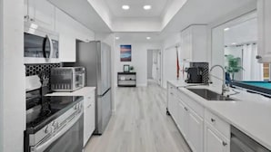 A modern kitchen with white cabinetry, a built-in oven, a microwave, and a sink. - Hot tub, Gazebo, Firepit Table Getaway Oasis House!!!! (Fort Myers)