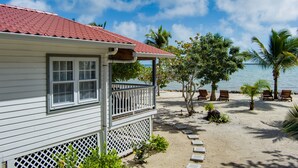 A white building with a red roof, a balcony, and a sandy beach with palm trees and lounge chairs. - Complete Beach Retreat: Cottage + Beachhouse (Placencia)