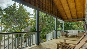 A wooden deck with a railing, lounge chairs, and a view of palm trees and a beach.