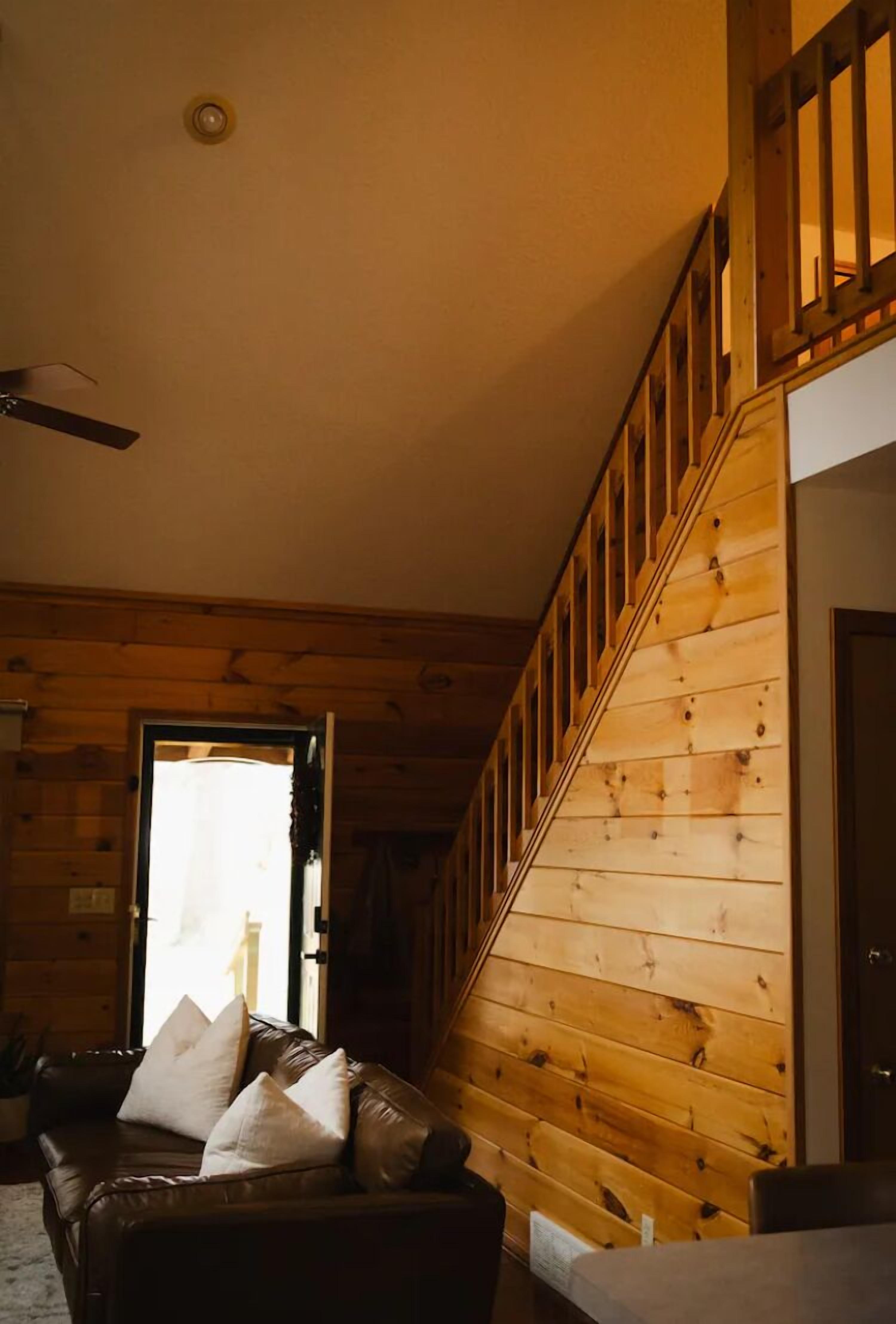 A wooden interior with a staircase, a leather sofa, and a door leading outside.