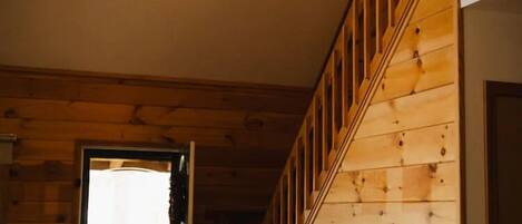 A wooden interior with a staircase, a leather sofa, and a door leading outside.