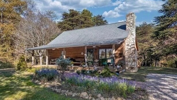 Une cabane rustique avec une cheminée en pierre, un revêtement extérieur en bois et une véranda dotée de meubles d’extérieur.