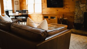 Un salon chaleureux avec un canapé en cuir marron, une cheminée en pierre et un téléviseur fixé au mur.