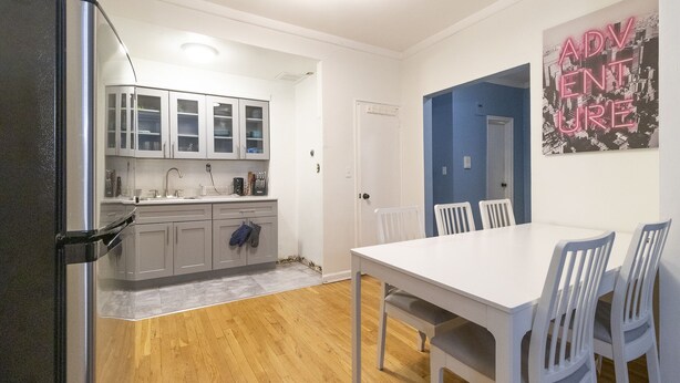 A modern kitchen with white cabinets, a stainless steel refrigerator, and a wooden floor. There is a dining area with a white table and chairs, and a blue door leading to another room. - Amazing 2 BR on Upper East Side NYC (New York)