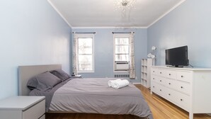 A bedroom with a bed, a dresser, a television, and two windows with curtains. - Amazing 2 BR on Upper East Side NYC (New York)