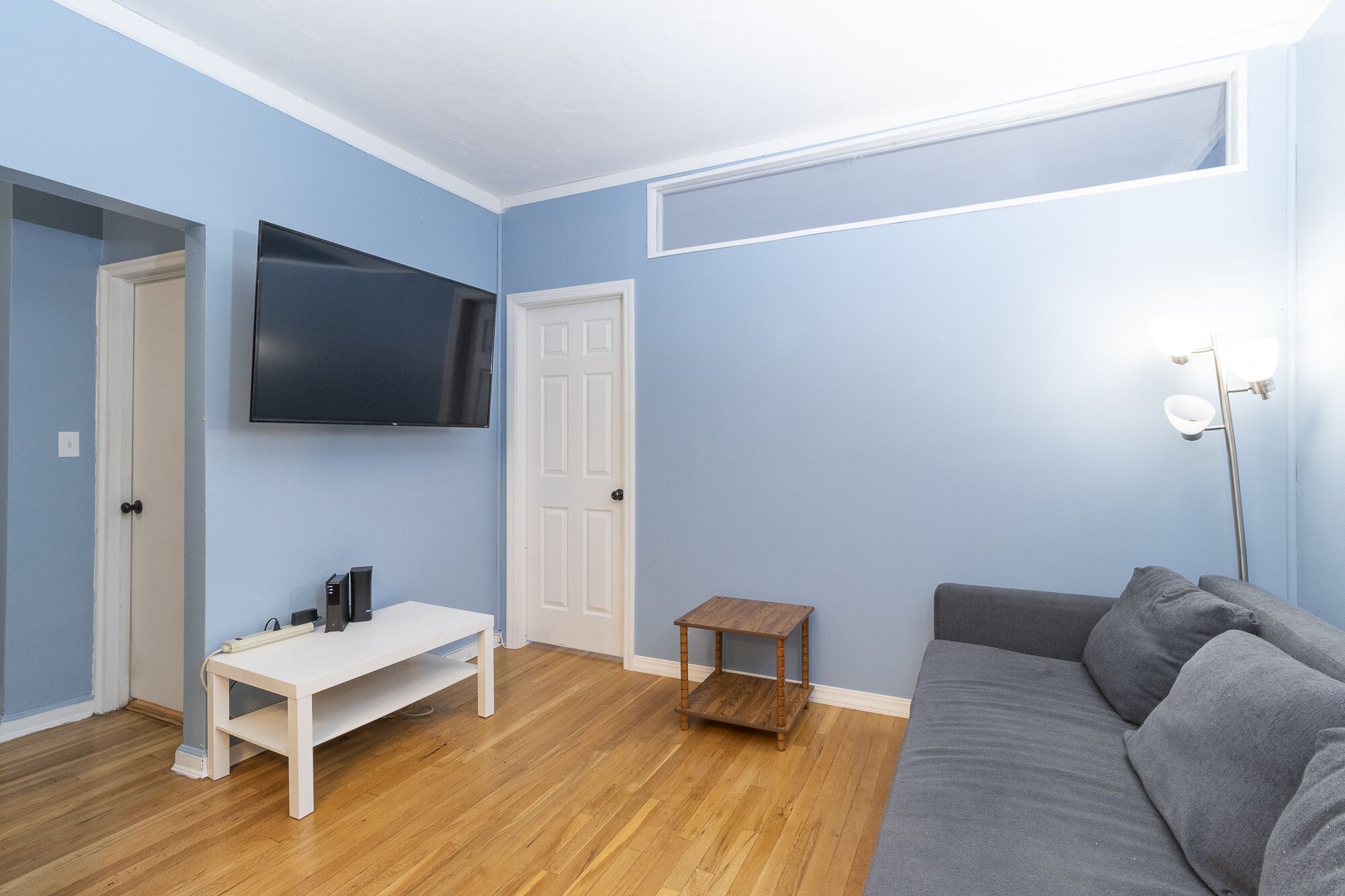 A living room with a grey sofa, a white TV stand, and a small wooden table.